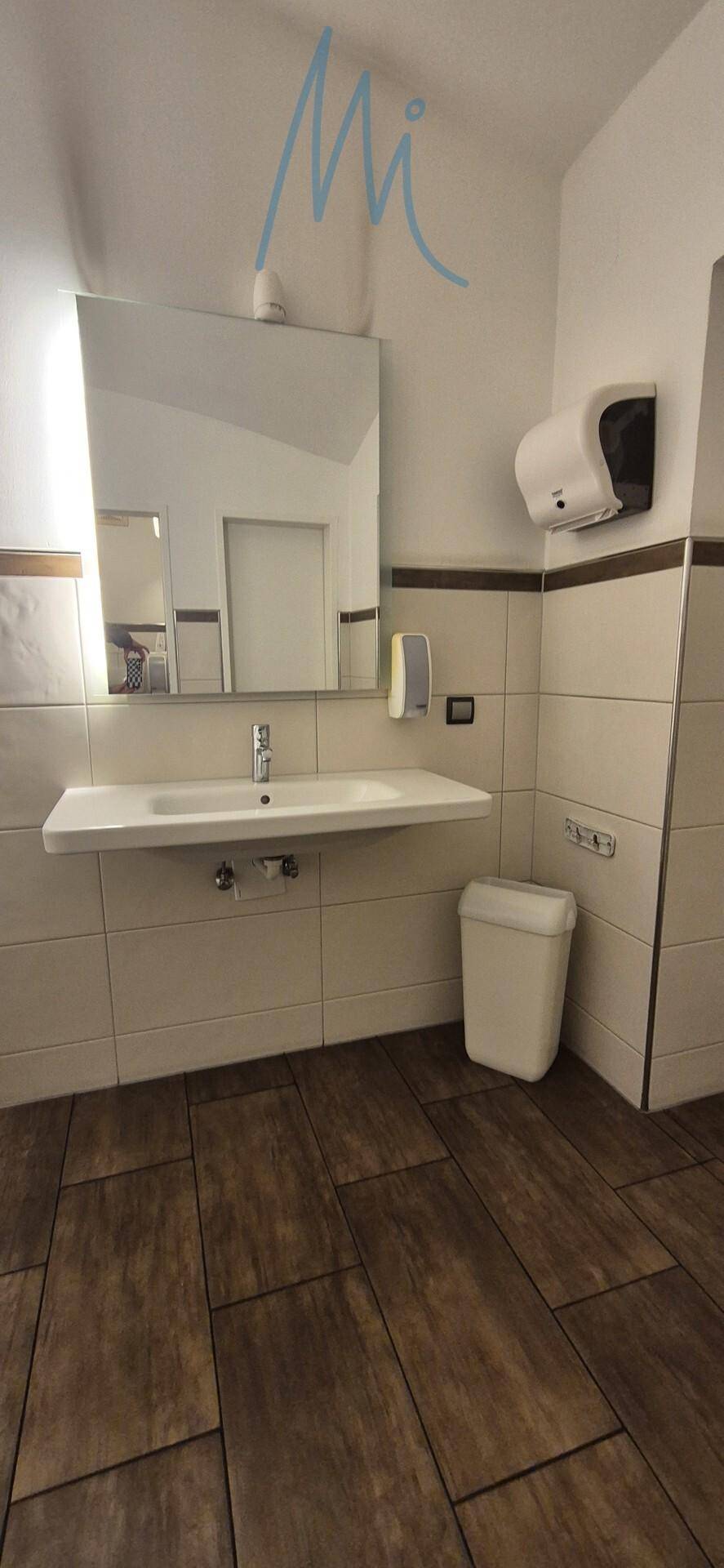 Moderner Waschbereich in einer öffentlichen Toilette mit großem Spiegel, Waschbecken und Handtrockner.