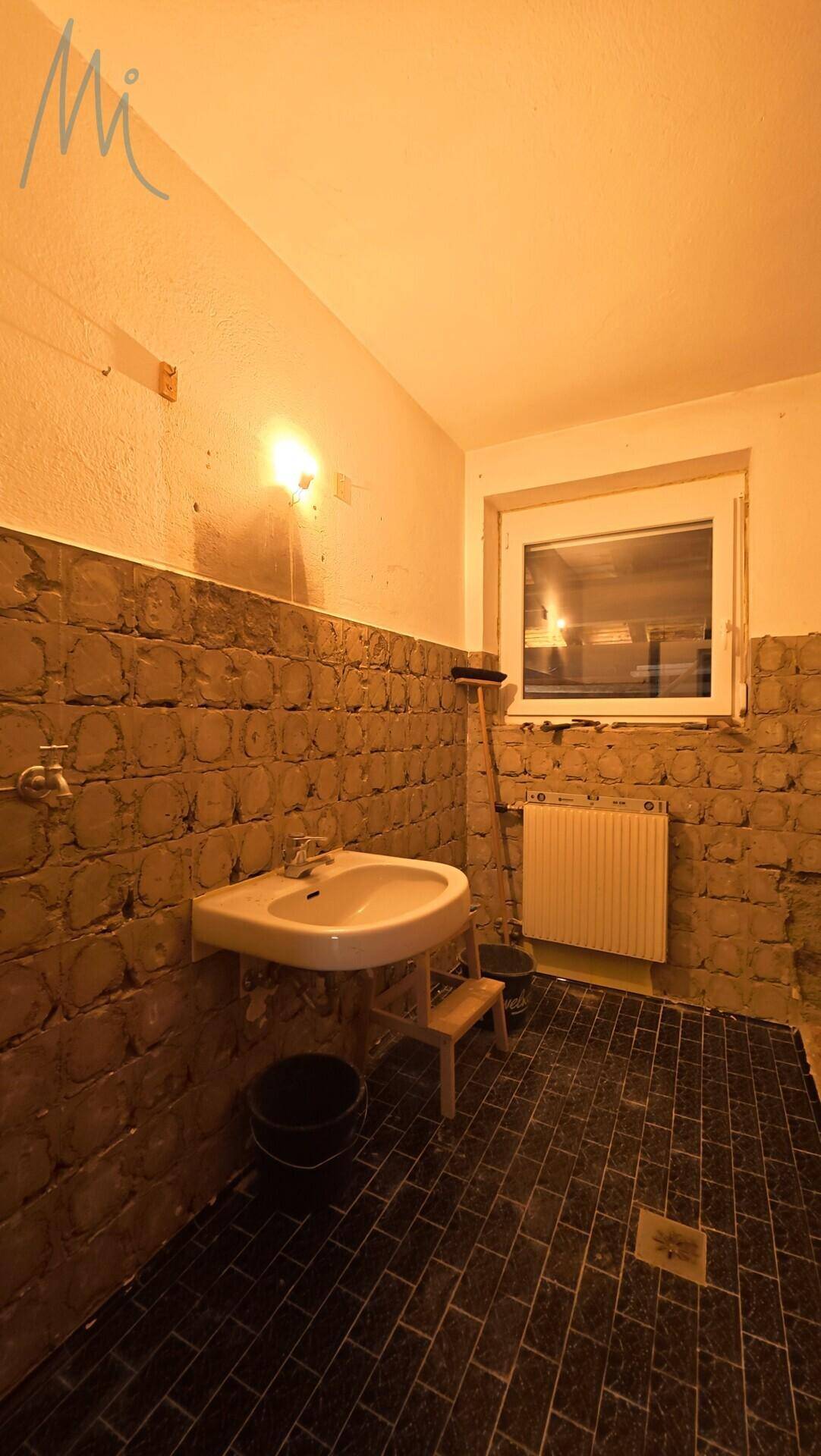 Badezimmer in Renovierung mit Fliesenboden, Waschbecken und Fenster.