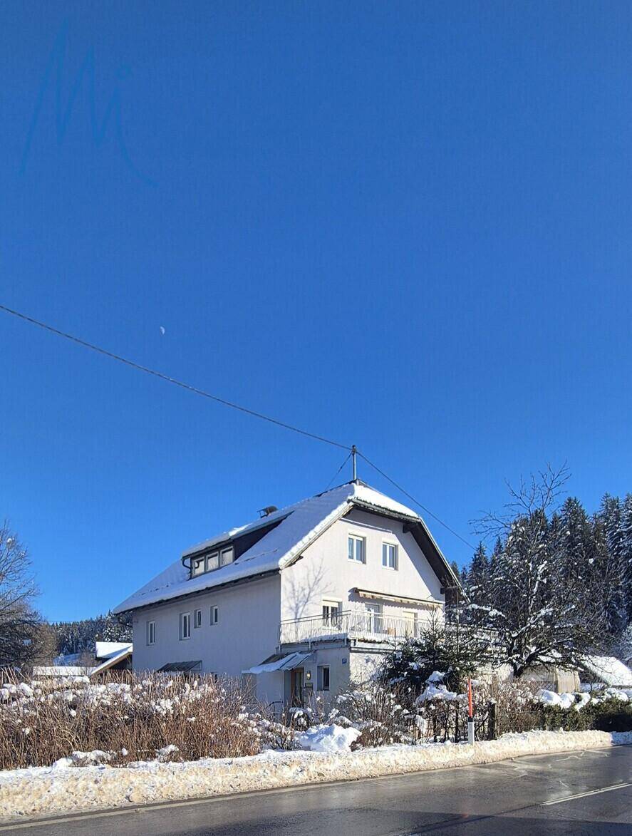 Winteransicht des Hauses mit schneebedecktem Dach und Bäumen vor klarem blauen Himmel.