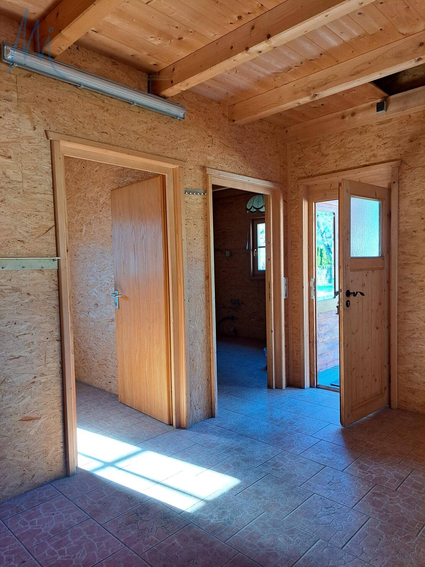 Innenraum des Holzgebäudes mit Holzwänden, Fliesenboden und mehreren Türen.