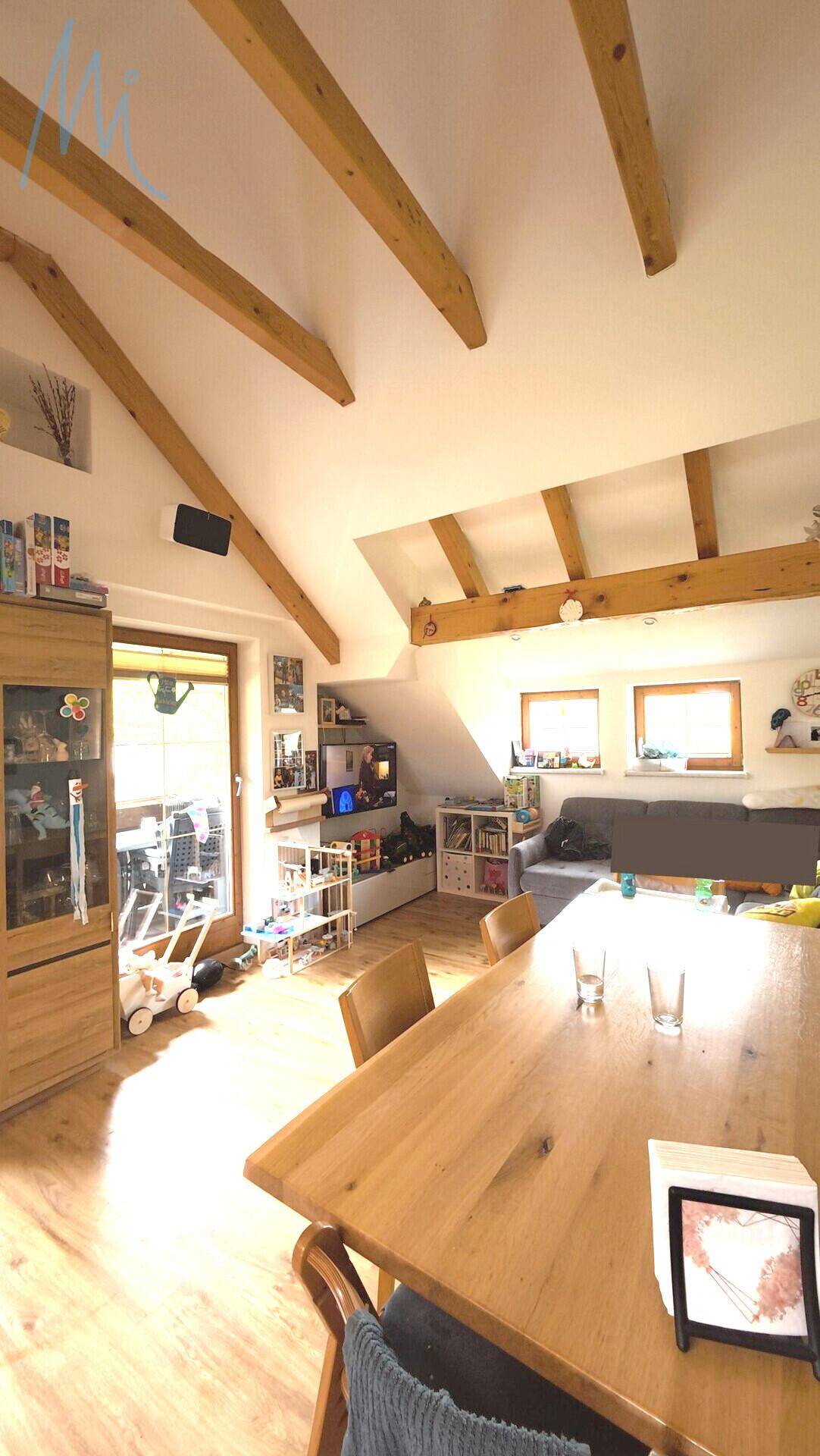 Heller Wohn-Essbereich mit Holzbalken, Holzboden und Zugang zum Balkon.