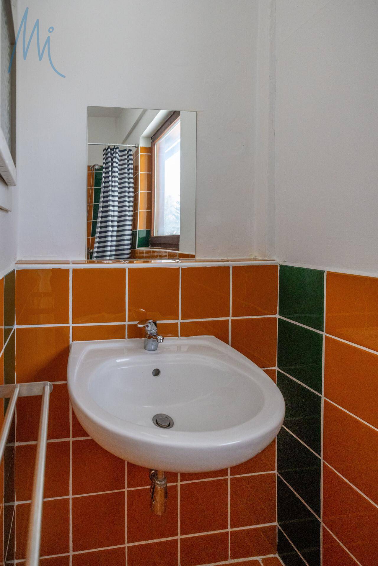 Badezimmer mit Waschbecken und orange-grünen Fliesen an den Wänden, einem Spiegel und einem Fenster.