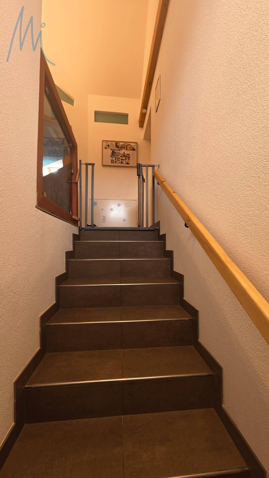 Treppenhaus mit dunklen Fliesenstufen und Holzhandlauf, das in die oberen Stockwerke führt.