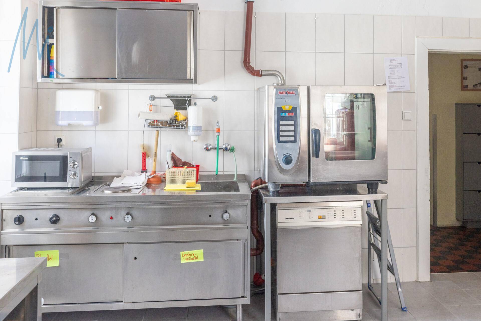 Professionelle Großküche mit Edelstahlgeräten, Mikrowelle und Spülmaschine, bereit für den Betrieb.