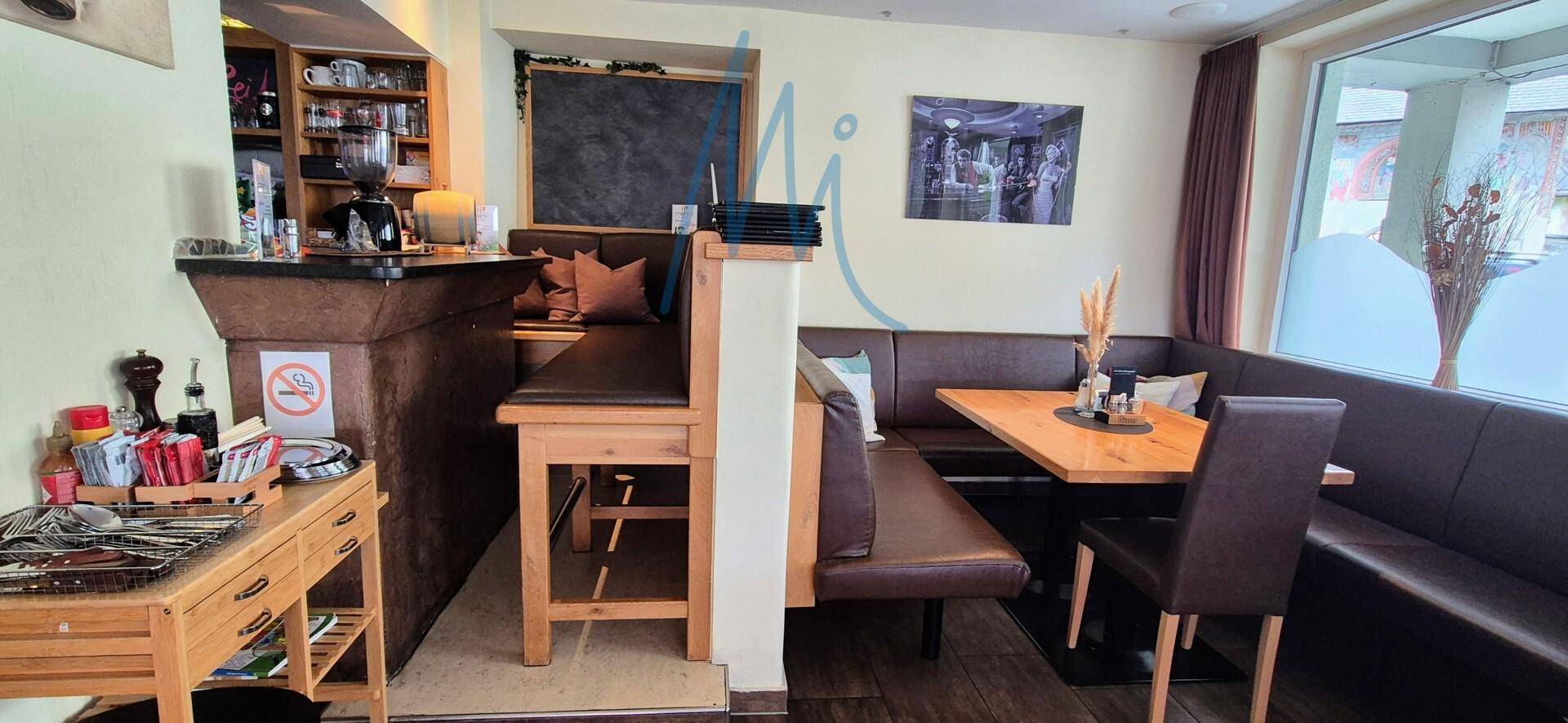 Eckbereich eines Restaurants mit bequemen Sitzbänken, Holztischen und großen Fenstern für natürliches Licht.