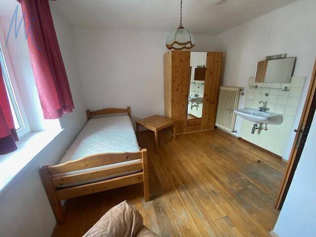 Einfaches Schlafzimmer mit Holzboden, Einzelbett, Kleiderschrank und Waschbecken.