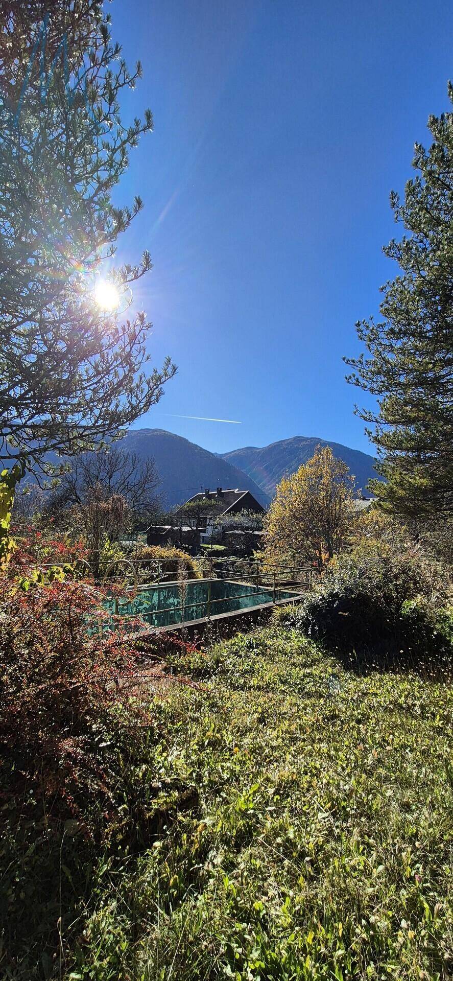 Weitblick auf ein Haus und die umliegende Berglandschaft durch die Baumwipfel.