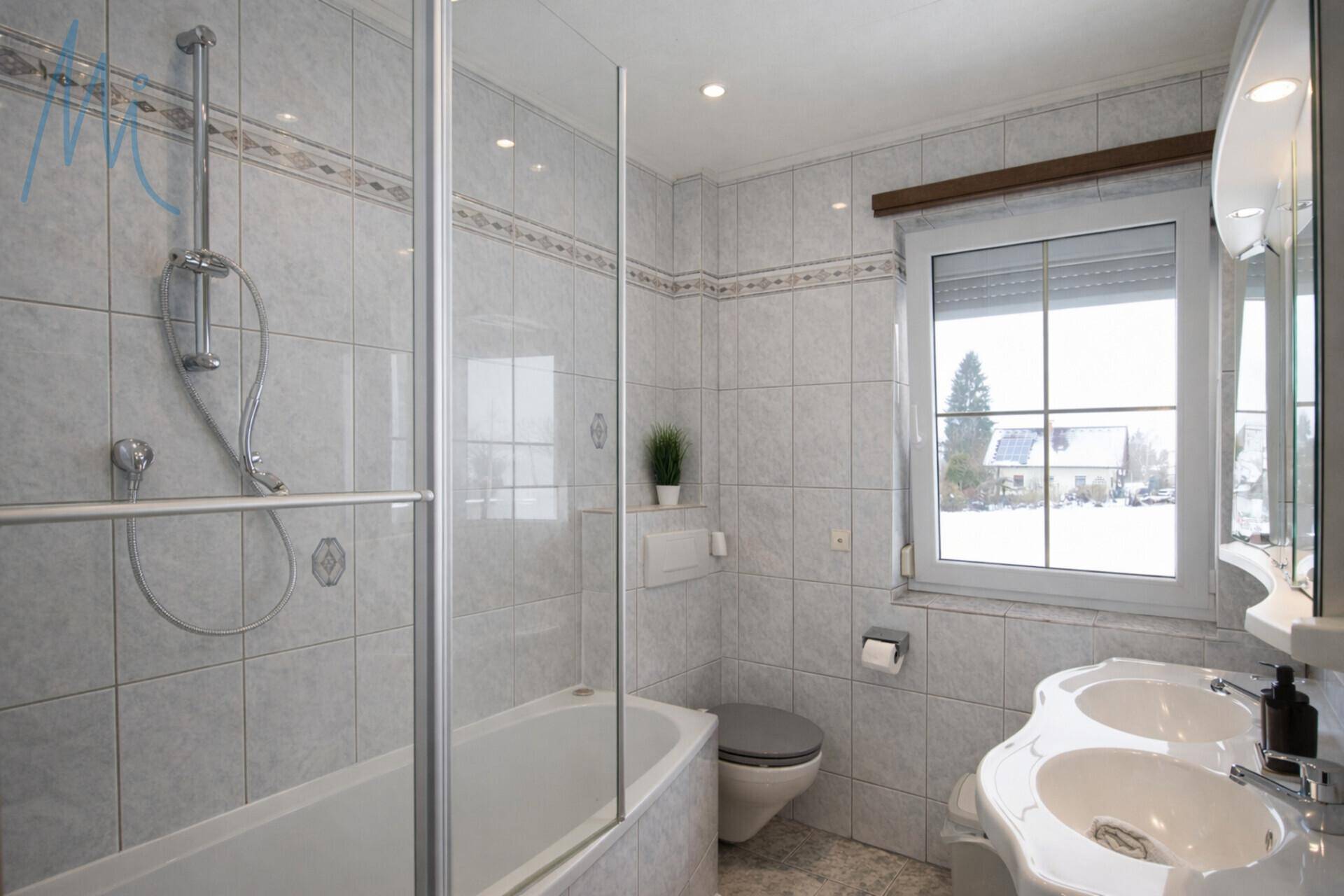 Gefliestes Badezimmer mit Doppelwaschbecken, Badewanne und Duschabtrennung.