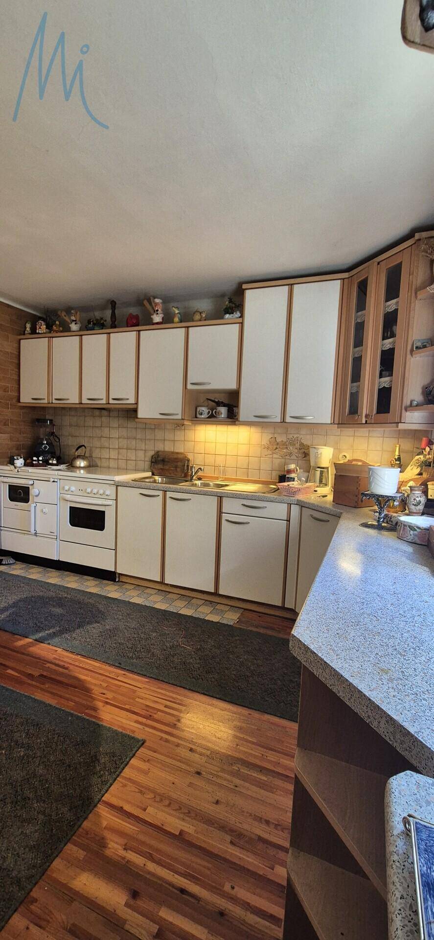 Funktionale Küche mit weißen und holzfarbenen Schränken, Fliesenrückwand und Arbeitsplatte.