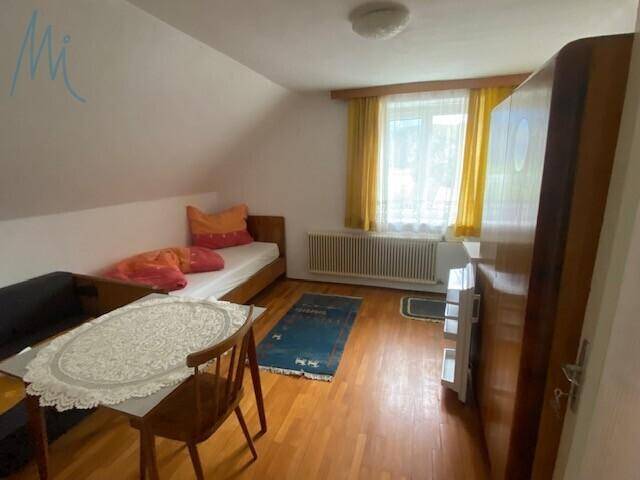 Helles Schlafzimmer mit Holzboden, Einzelbett und einem kleinen Tisch unter dem Fenster.