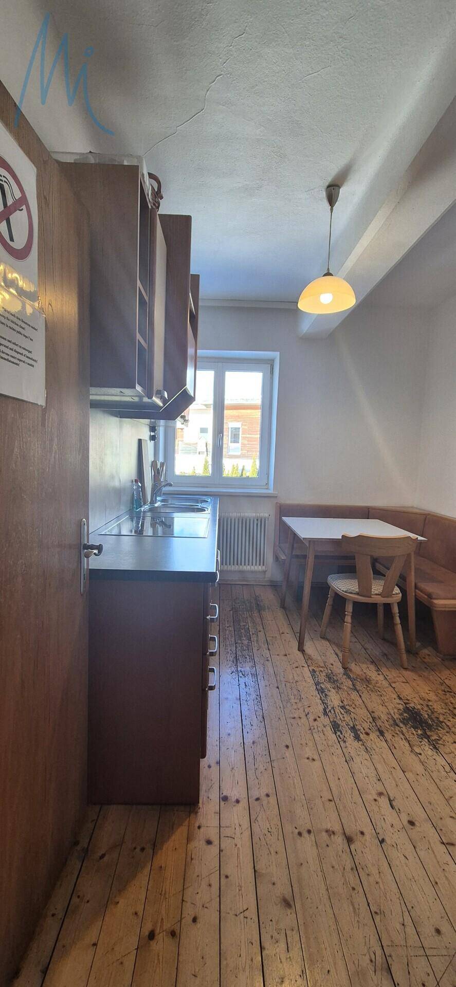 Rustikale Küche mit Holzboden, Spüle und gemütlicher Essecke am Fenster.