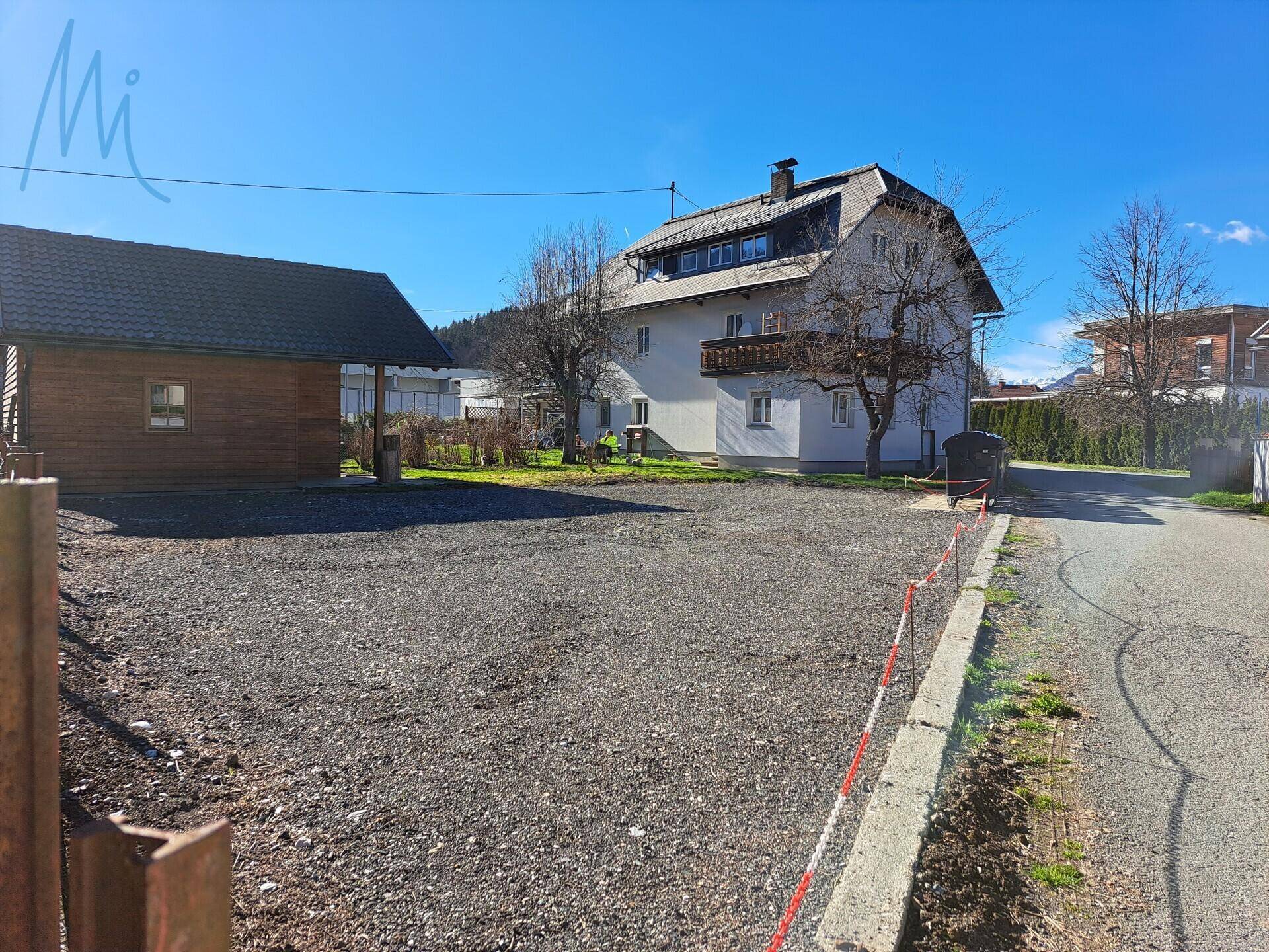Das Anwesen umfasst ein Hauptgebäude und ein Nebengebäude mit großem Schotterparkplatz unter blauem Himmel.