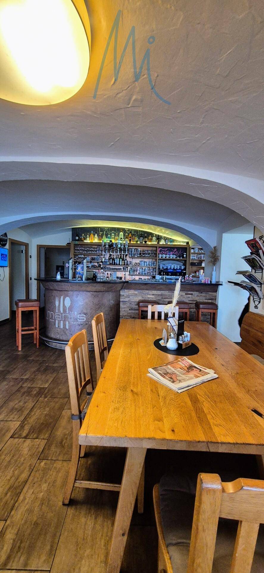 Gemütlicher Restaurantbereich mit Holztischen, Stühlen und einer gut ausgestatteten Bar im Hintergrund.