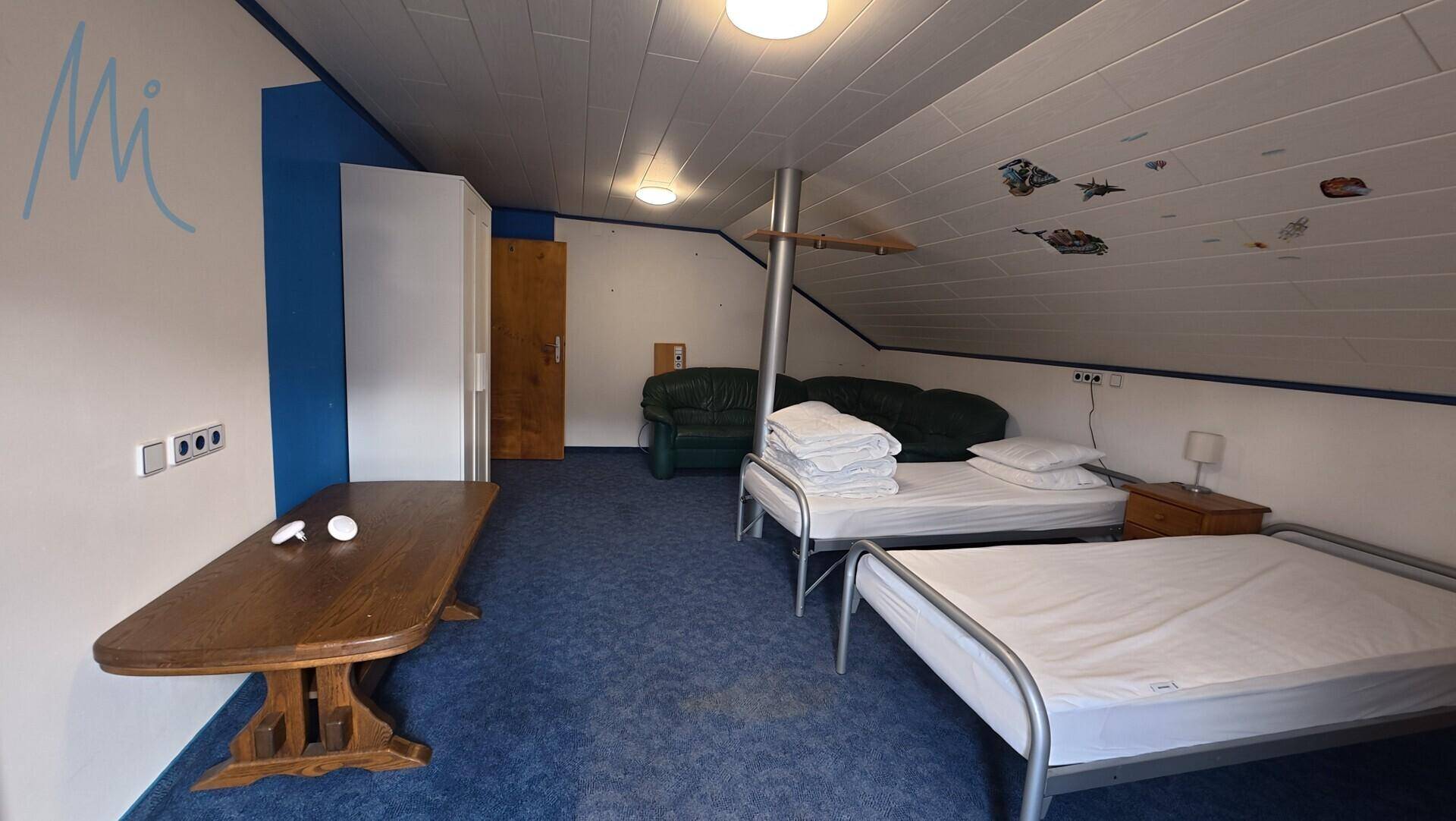 Dachgeschoss-Schlafzimmer mit zwei Einzelbetten, blauem Teppich und Holztisch.