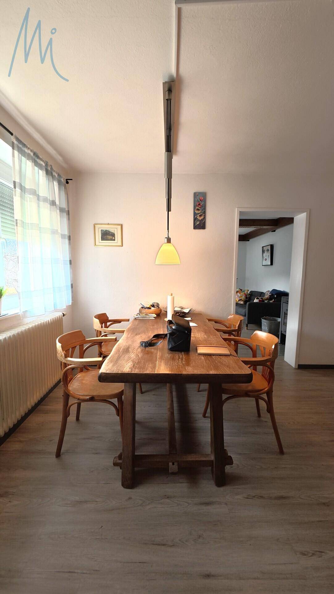 Gemütlicher Essbereich mit Holztisch, Stühlen und Blick ins Grüne durch das Fenster.