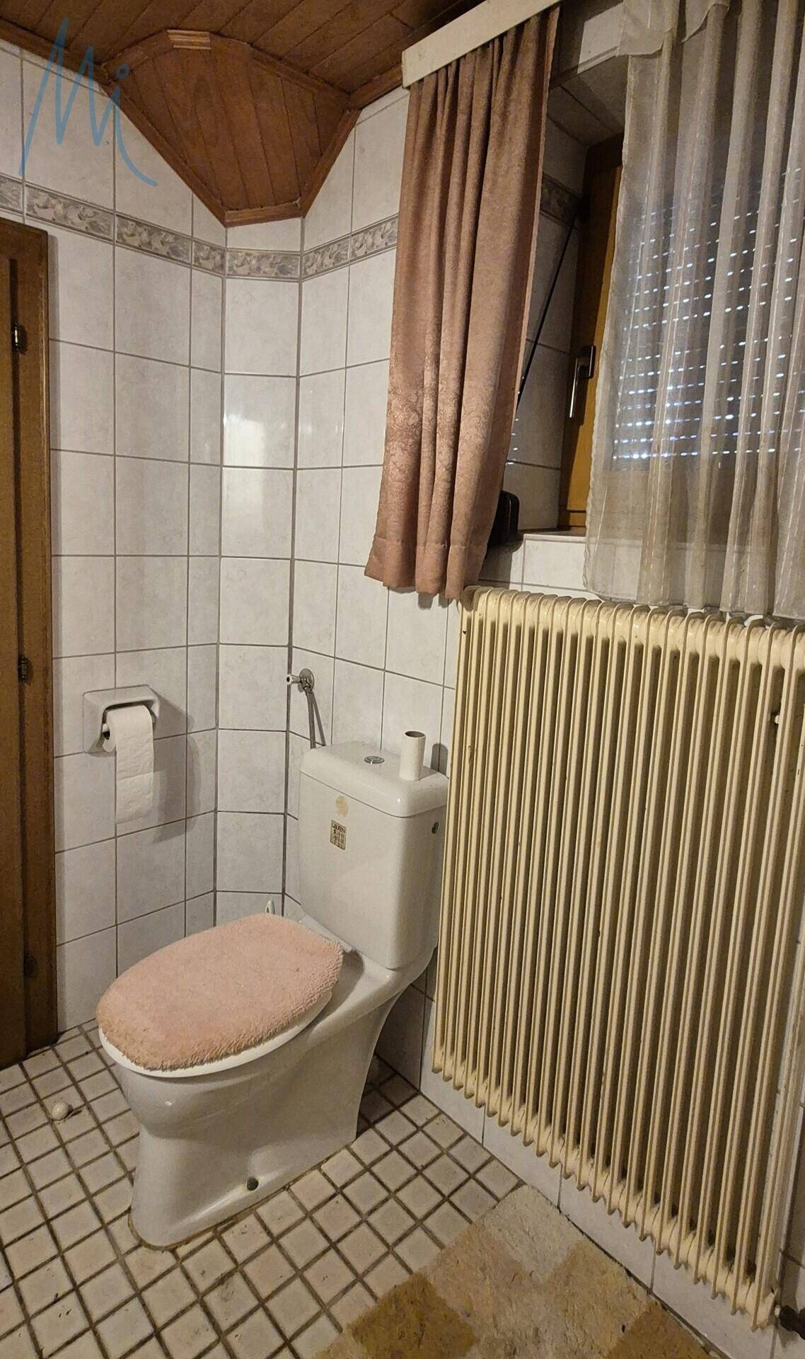 Separates WC mit Toilette, Heizkörper und gefliesten Wänden, inklusive Fenster.