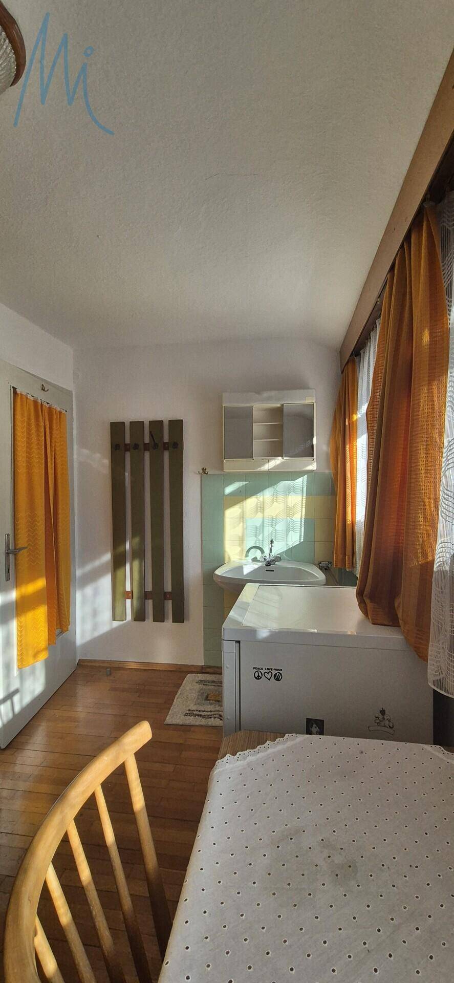 Raum mit Waschbecken, Kühlschrank und Fenster, ideal als kleine Küchenzeile nutzbar.