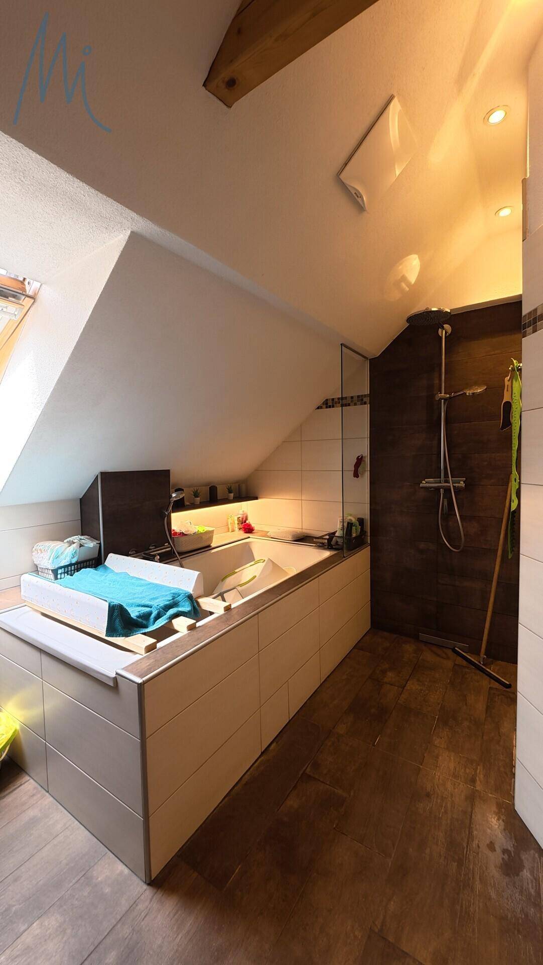 Badezimmer im Dachgeschoss mit Badewanne, Duschbereich und schräger Decke.