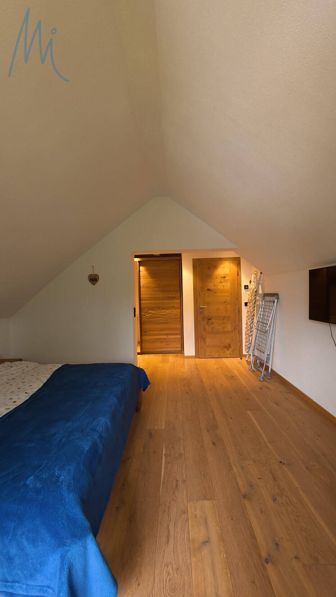Schlafzimmer im Dachgeschoss mit Holzboden, schräger Decke und Holztüren.