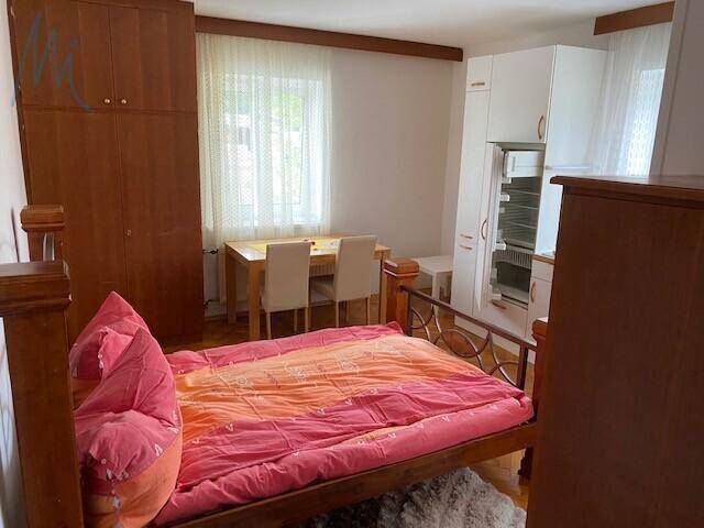 Gemütliches Schlafzimmer mit Holzbett, Esstisch und integrierter Küchenzeile unter dem Fenster.