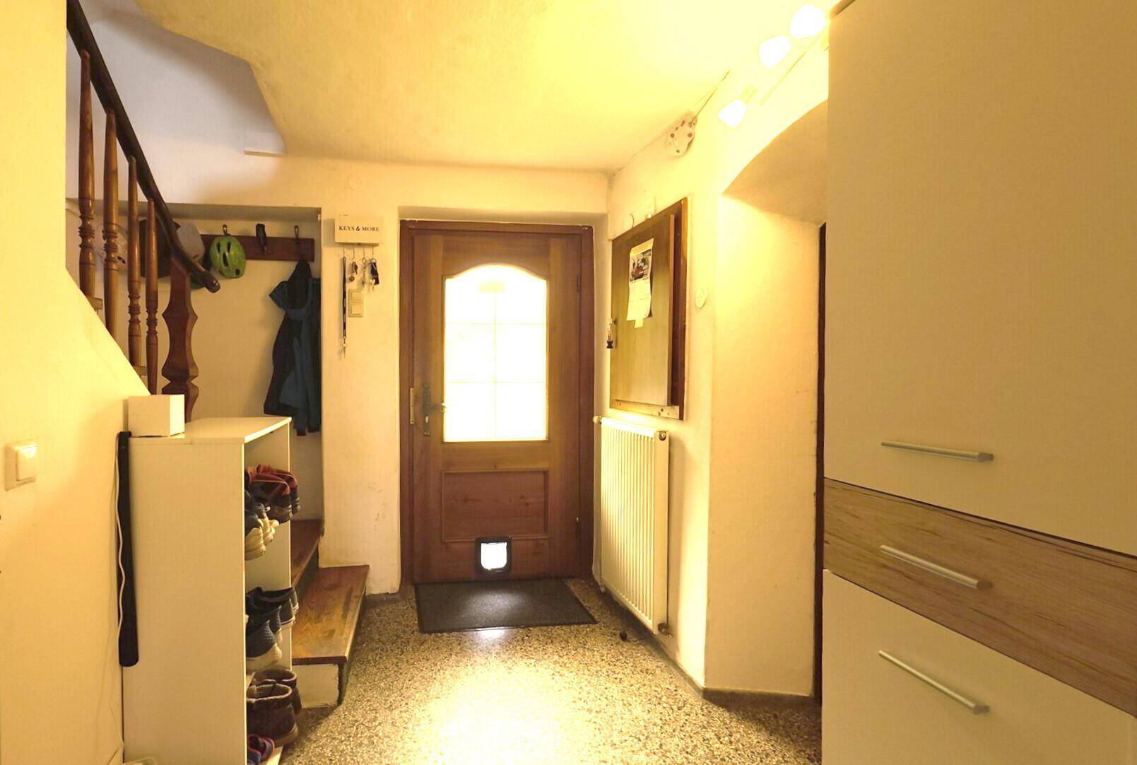 Heller Eingangsbereich mit Holztreppe, Schuhregal und einer Holztür mit Glaseinsatz.
