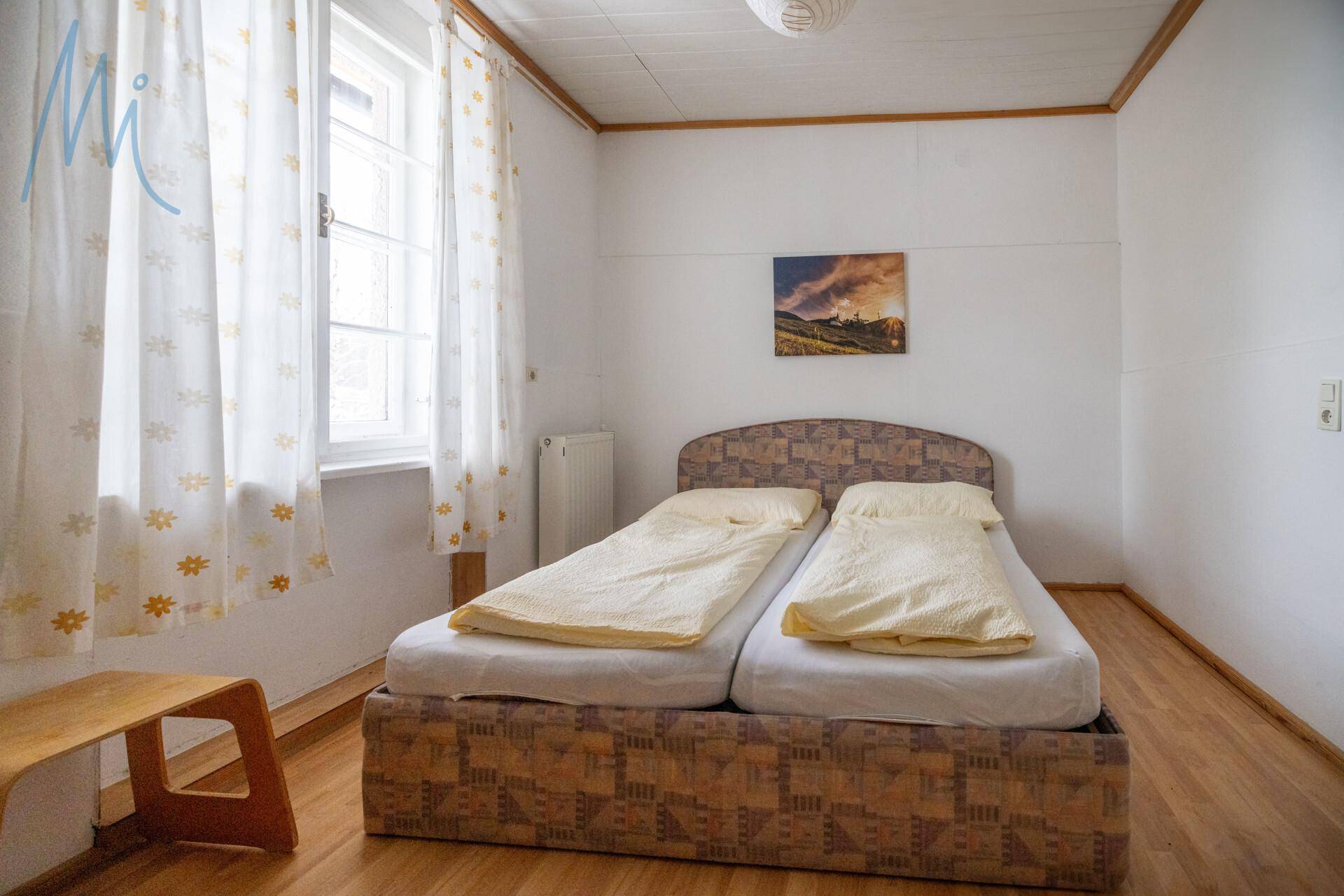 Schlafzimmer mit zwei Einzelbetten, die zu einem Doppelbett zusammengestellt sind, und einem Fenster mit gemusterten Vorhängen.