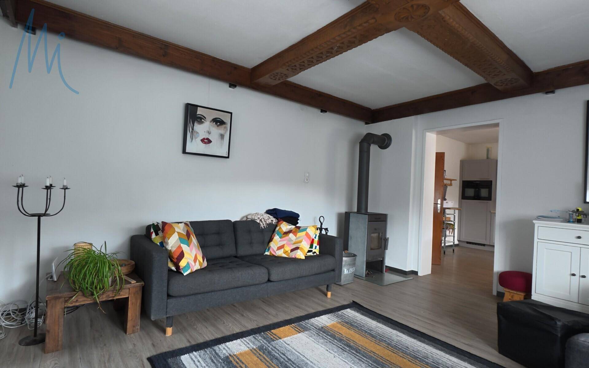 Helles Wohnzimmer mit Holzbalkendecke, Kaminofen und bequemen Sofas.