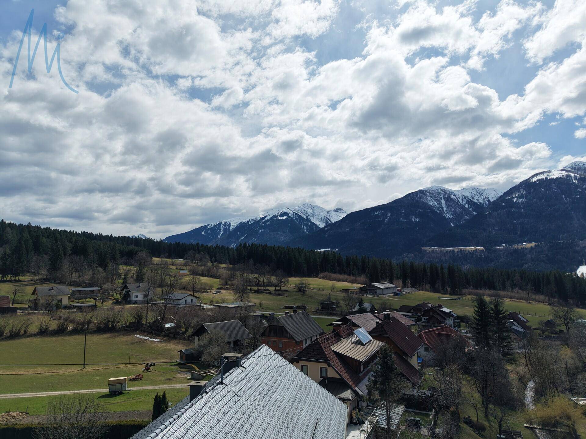 Weitläufiger Panoramablick über eine ländliche Siedlung mit schneebedeckten Bergen im Hintergrund.