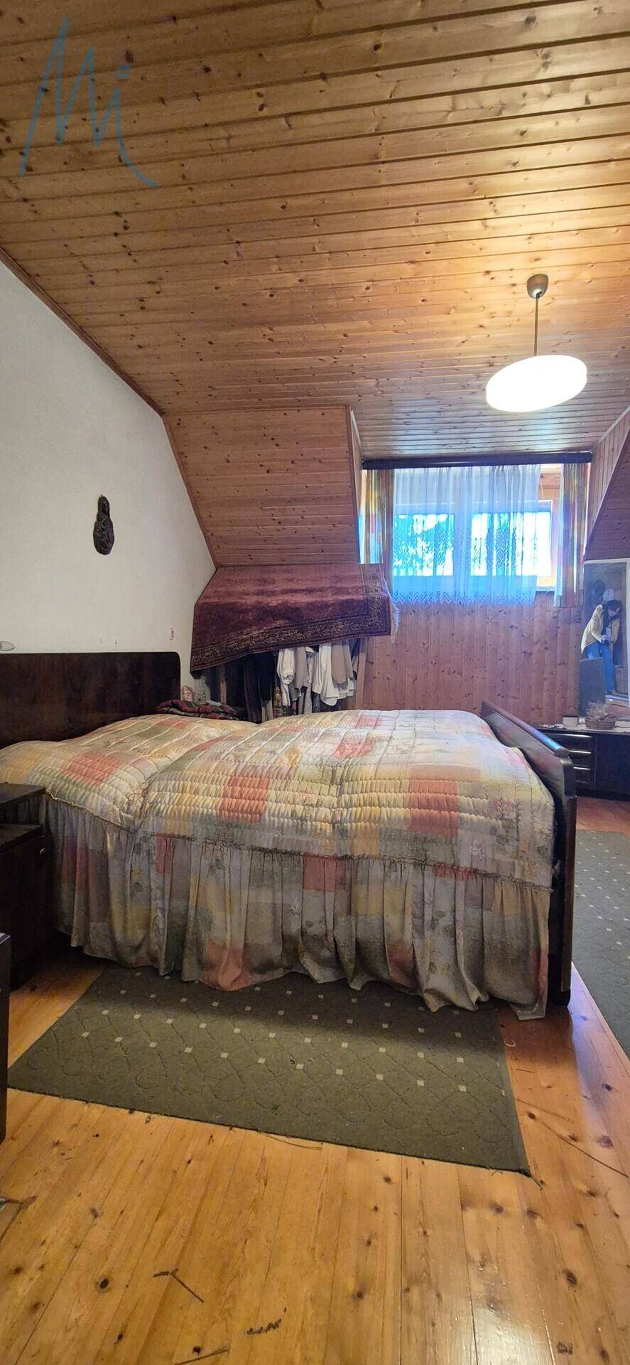 Schlafzimmer im Dachgeschoss mit Holzbalkendecke, Doppelbett und Blick ins Grüne.