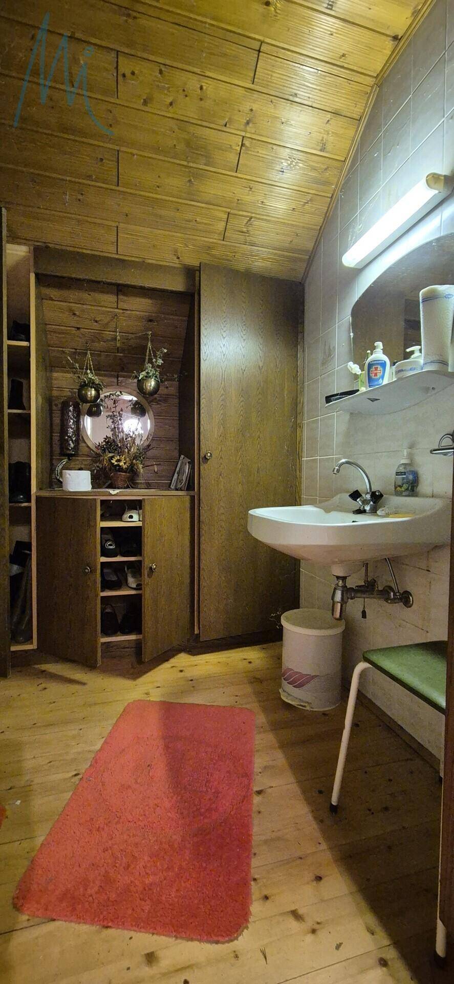 Badezimmer mit Waschbecken, Spiegel, Holzschränken und schräger Holzdecke.