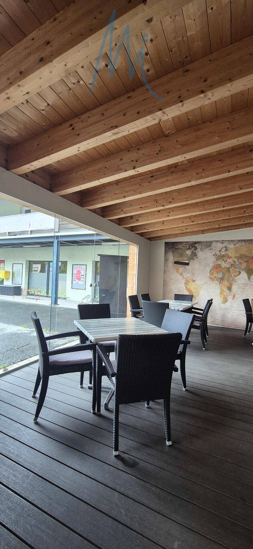 Überdachter Außenbereich mit Holzdielenboden, Holzbalkendecke und modernen Sitzgelegenheiten, ideal für Gäste.