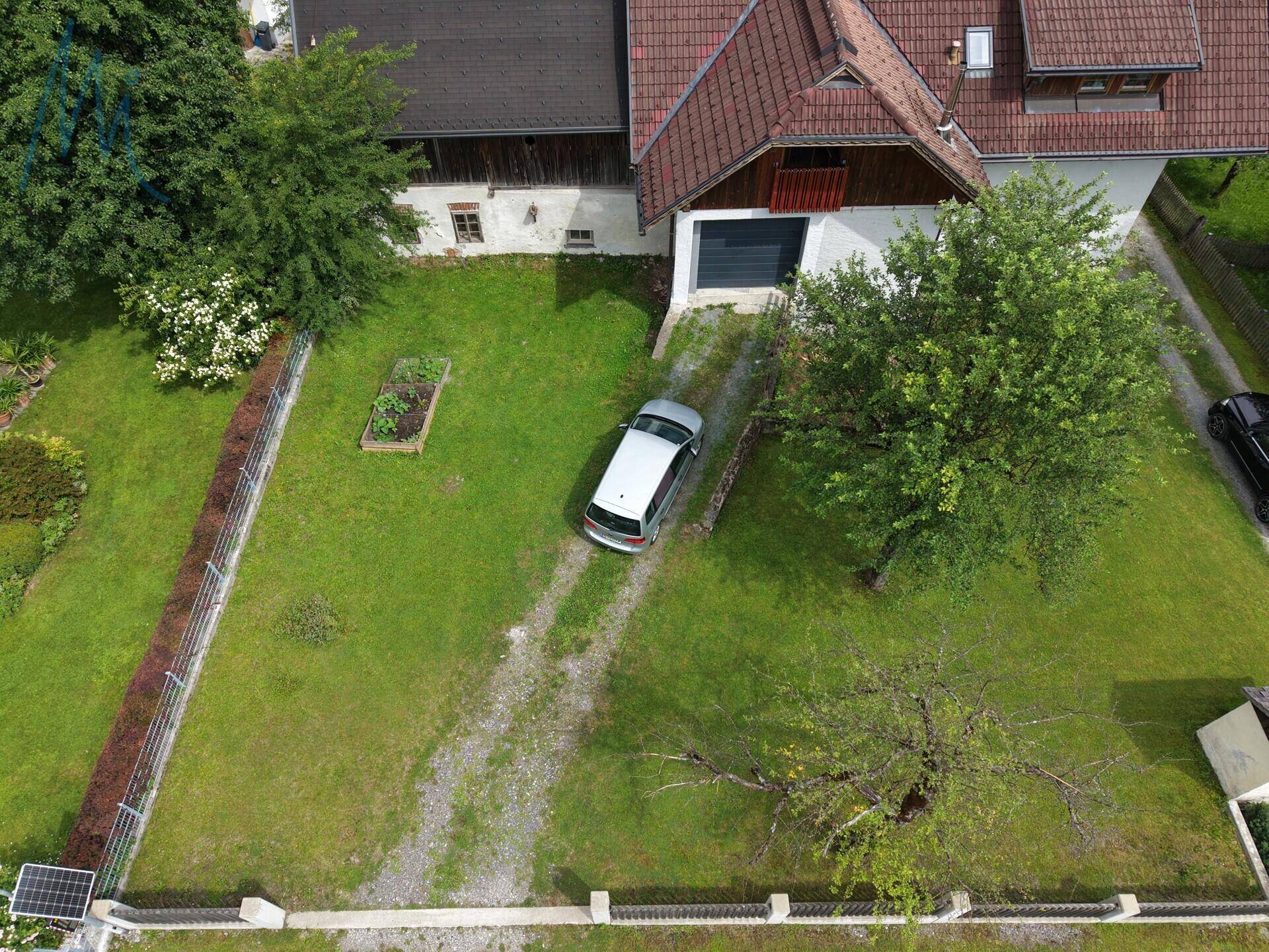 Luftaufnahme des Vorgartens mit Zufahrt und einem Teil des Hauses, umgeben von Bäumen und Rasen.