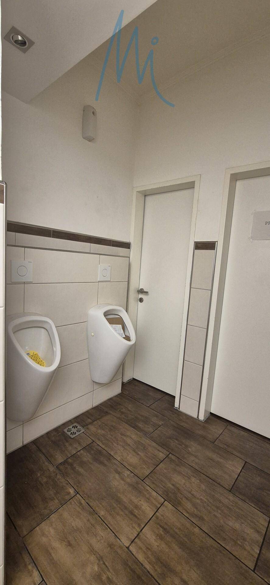 Herren-WC mit zwei Urinalen, Fliesenboden und weißen Wänden, sauber und funktional.