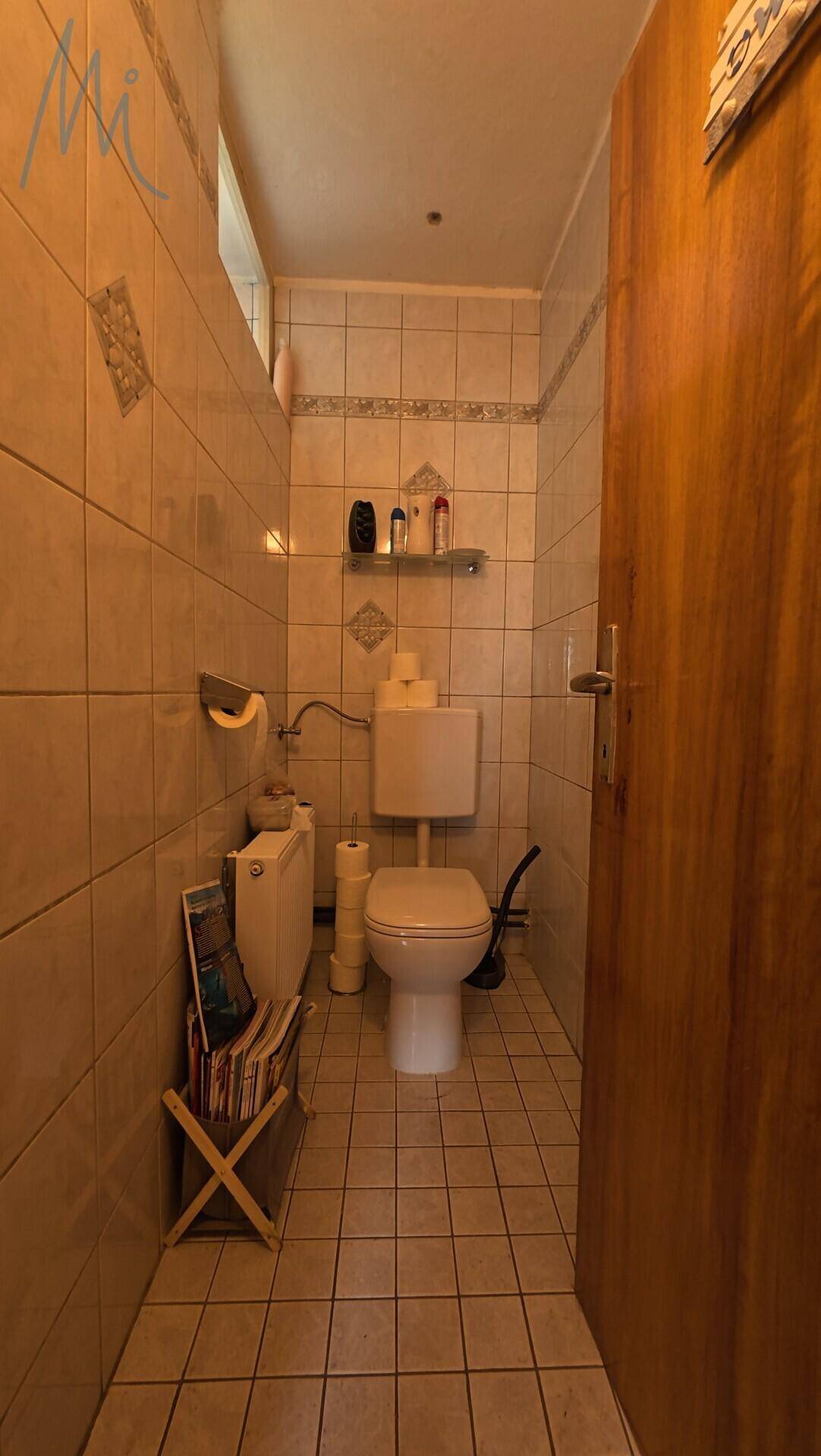 Separates WC mit Fliesenboden, Toilette und einem kleinen Fenster für Tageslicht.