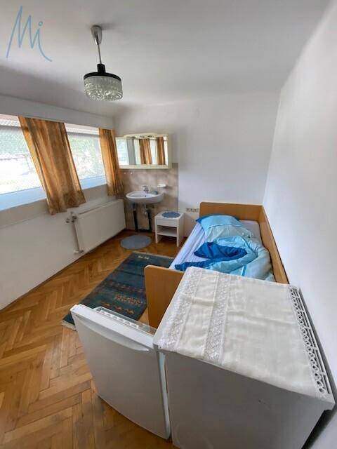 Schlafzimmer mit Einzelbett, Waschbecken und Spiegel, sowie einem kleinen Kühlschrank.