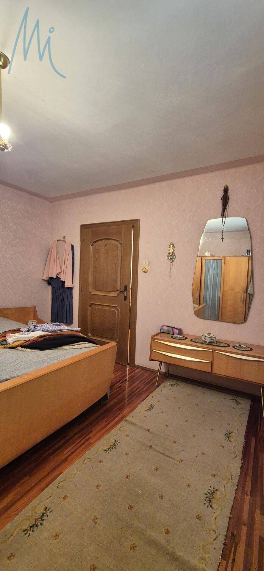 Schlafzimmer mit Bett, Holztür und einem Spiegel, der den Raum optisch vergrößert.