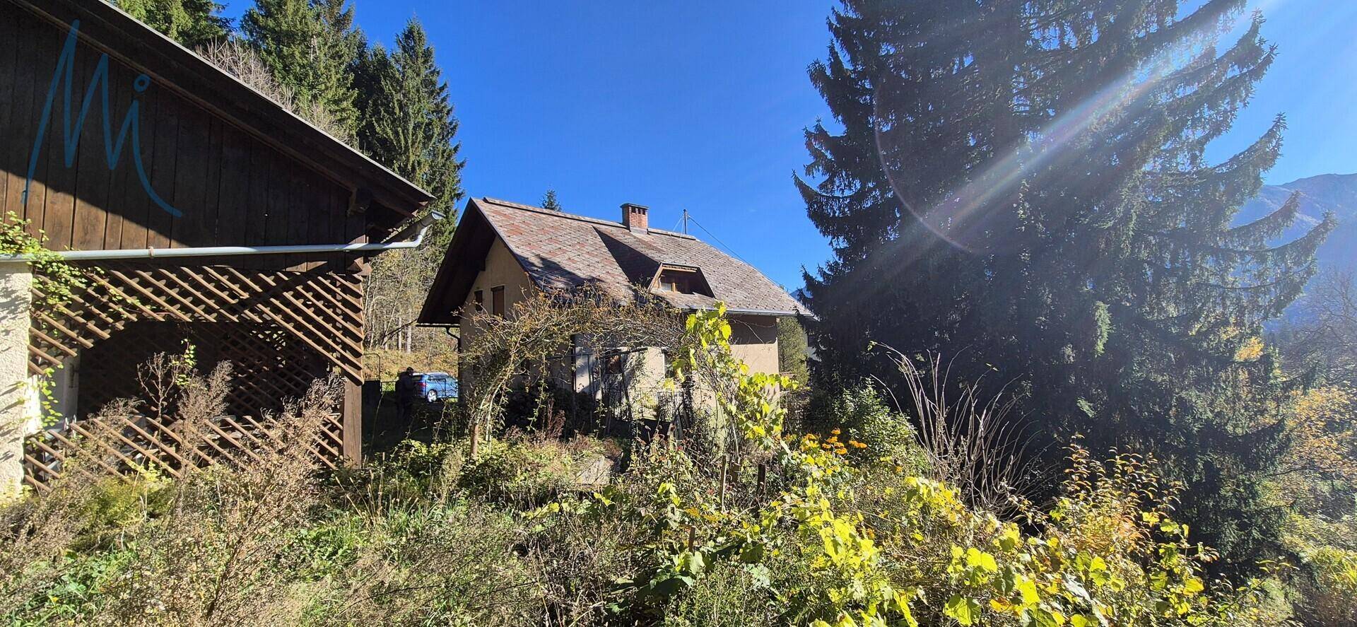 Rückansicht des Hauses und eines Nebengebäudes, eingebettet in eine bewaldete Hügellandschaft.