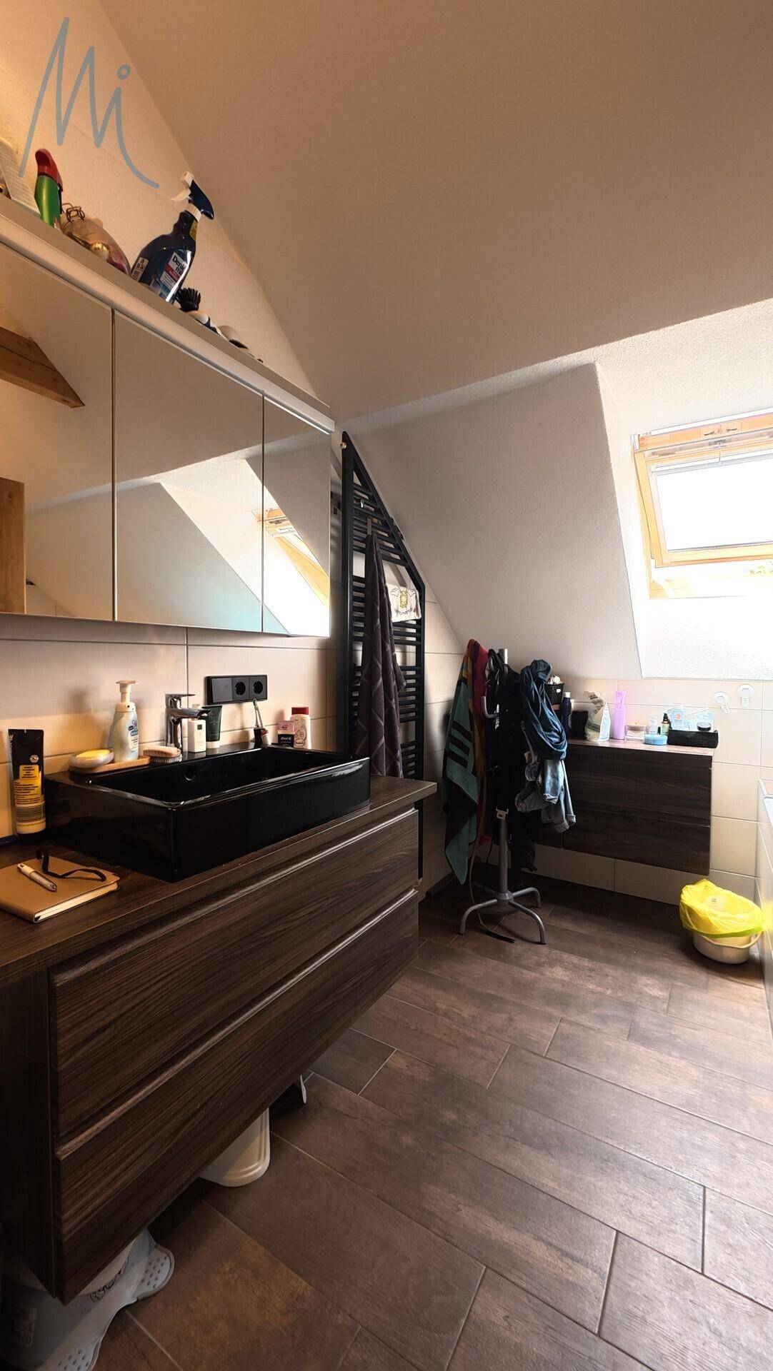 Modernes Badezimmer mit dunklem Waschtisch, Spiegelschrank und Dachfenster unter der Dachschräge.