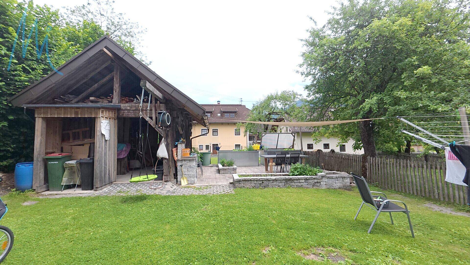 Gemütlicher Gartenbereich mit Holzschuppen, gepflasterter Terrasse und Wäscheleine im Freien.