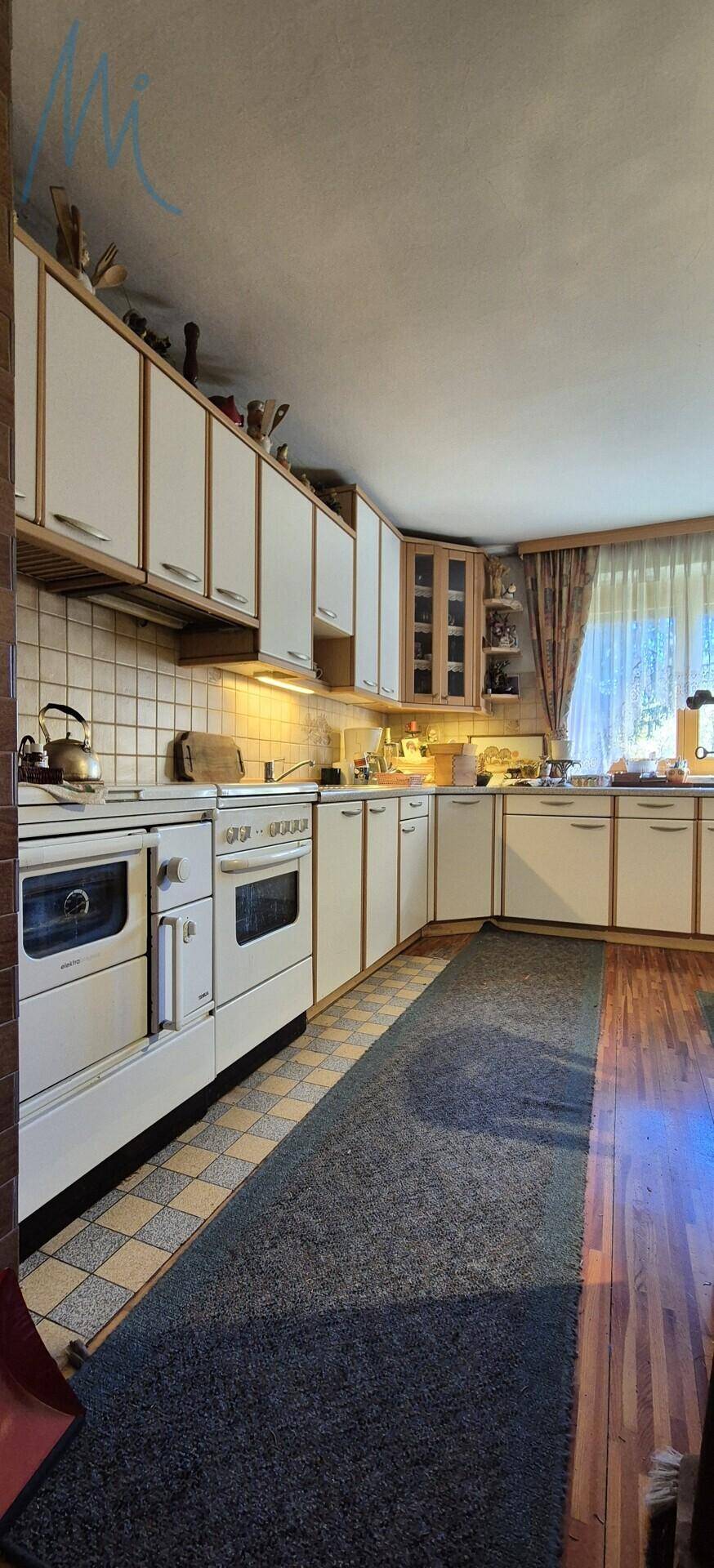 Traditionelle Küche mit weißen Schränken, Holzdetails und einem Teppichläufer auf dem Boden.