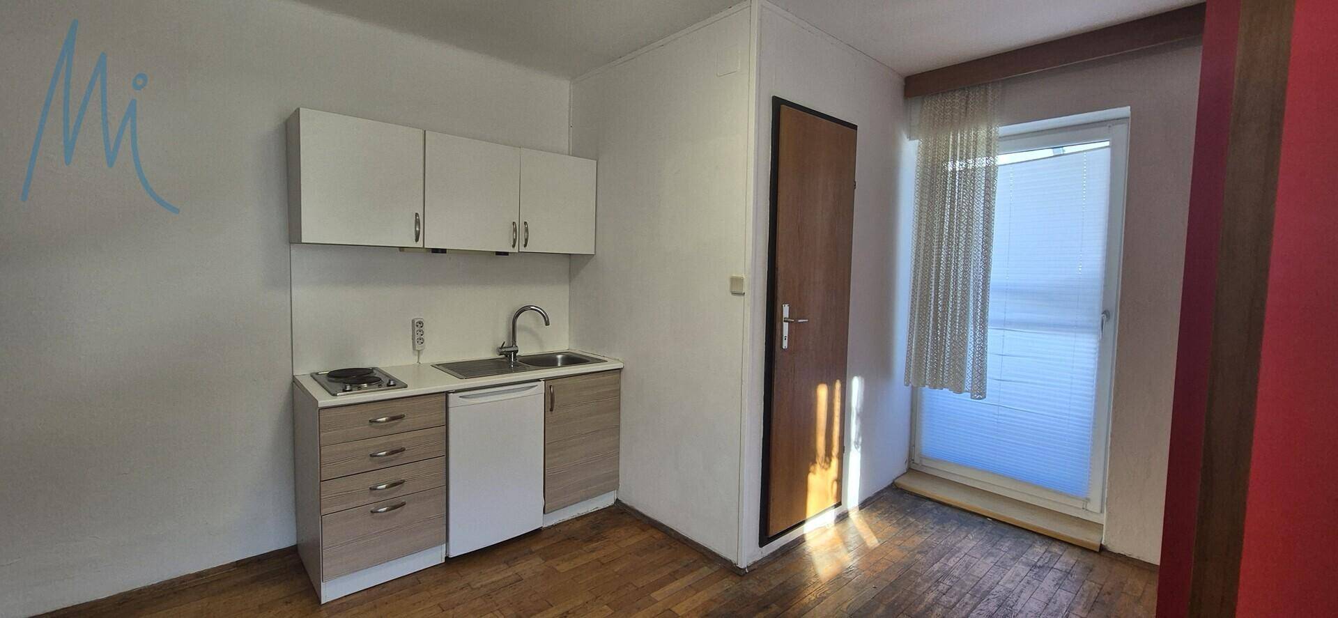 Kompakte Küchenzeile mit Spüle und Kochfeld, daneben eine Tür nach draußen.