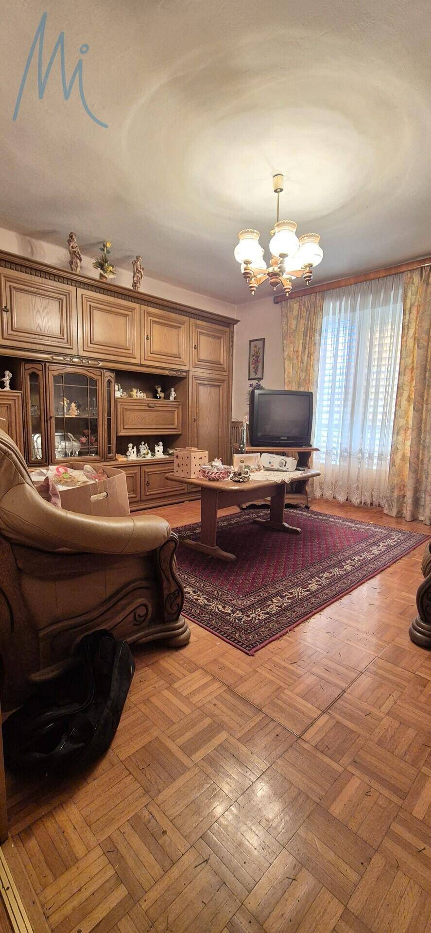 Geräumiges Wohnzimmer mit Parkettboden, traditionellen Holzmöbeln und einem großen Teppich.