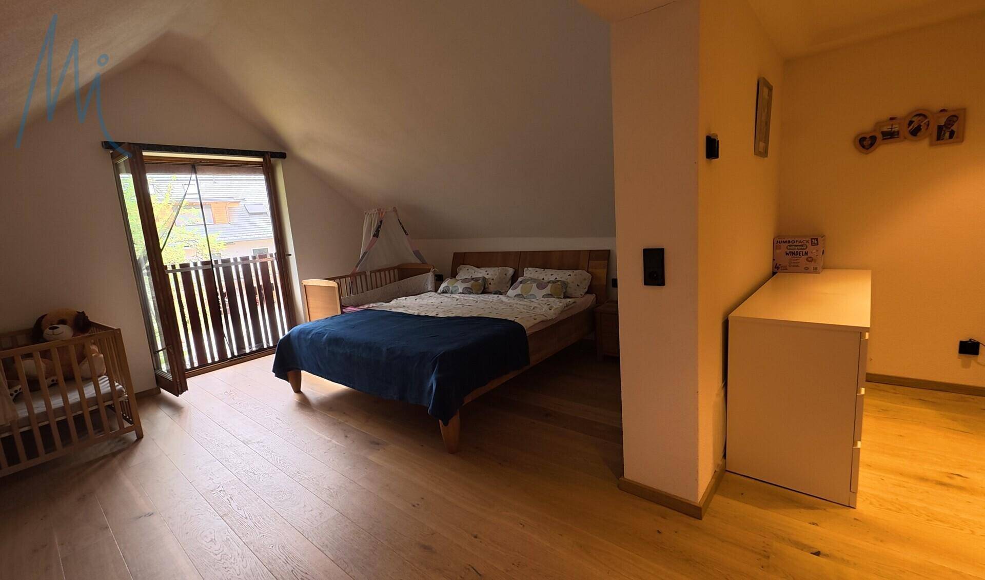Schlafzimmer im Dachgeschoss mit Holzboden, schräger Decke und Zugang zu einem französischen Balkon.