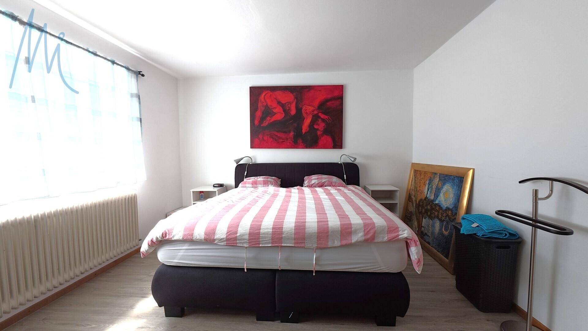 Helles Schlafzimmer mit Doppelbett, rotem Kunstwerk und großem Fenster.