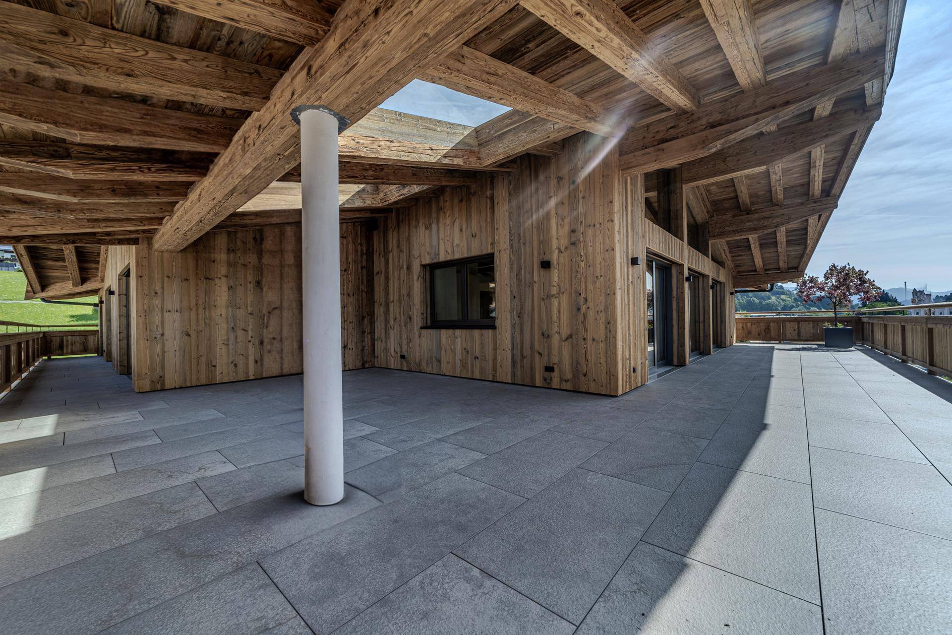 Große, sonnige Terrasse mit Steinplattenboden und Holzbalkenkonstruktion, ideal für Entspannung im Freien.