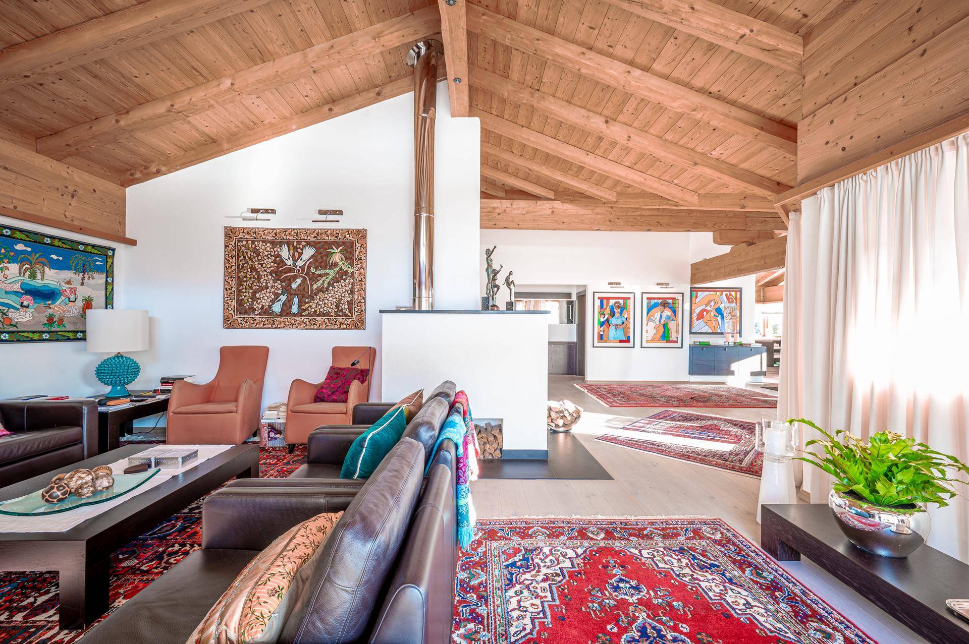Gemütliches Wohnzimmer mit Holzbalkendecke, Ledersofas und farbenfrohen Teppichen in offenem Design.