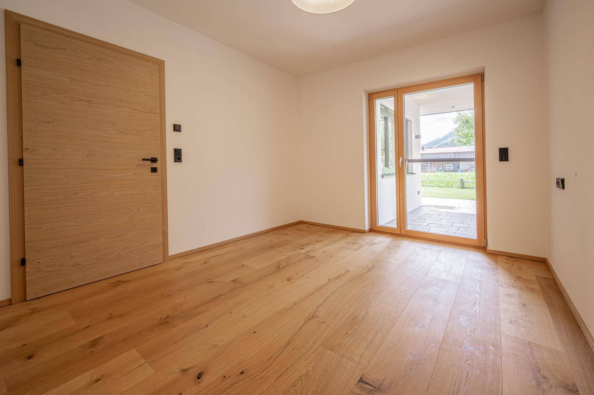 Helles Zimmer mit Eichenparkettboden und Zugang zu einer Terrasse oder einem Balkon.