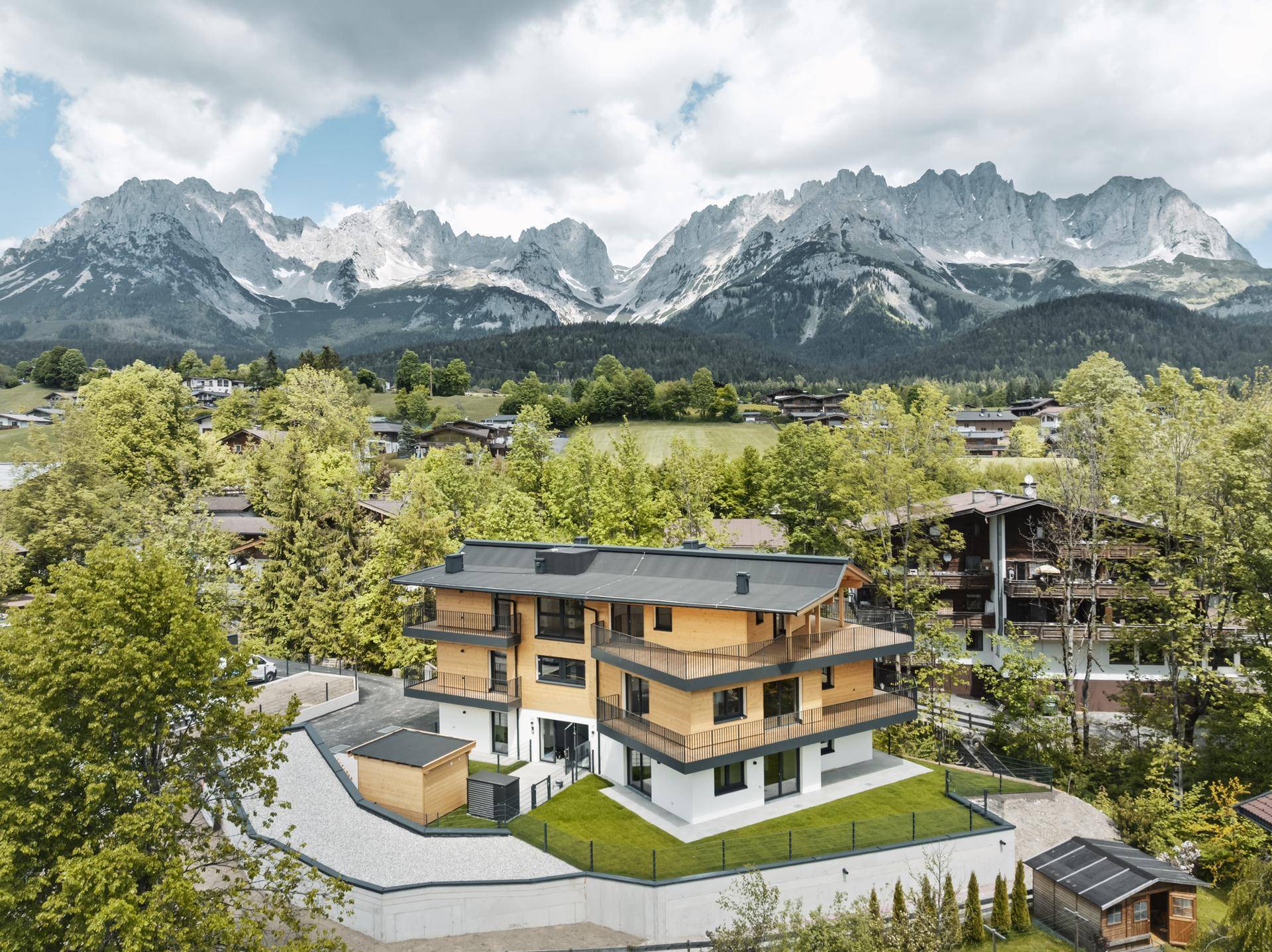 Luftaufnahme eines modernen Wohngebäudes mit Holzfassade und beeindruckendem Bergblick.