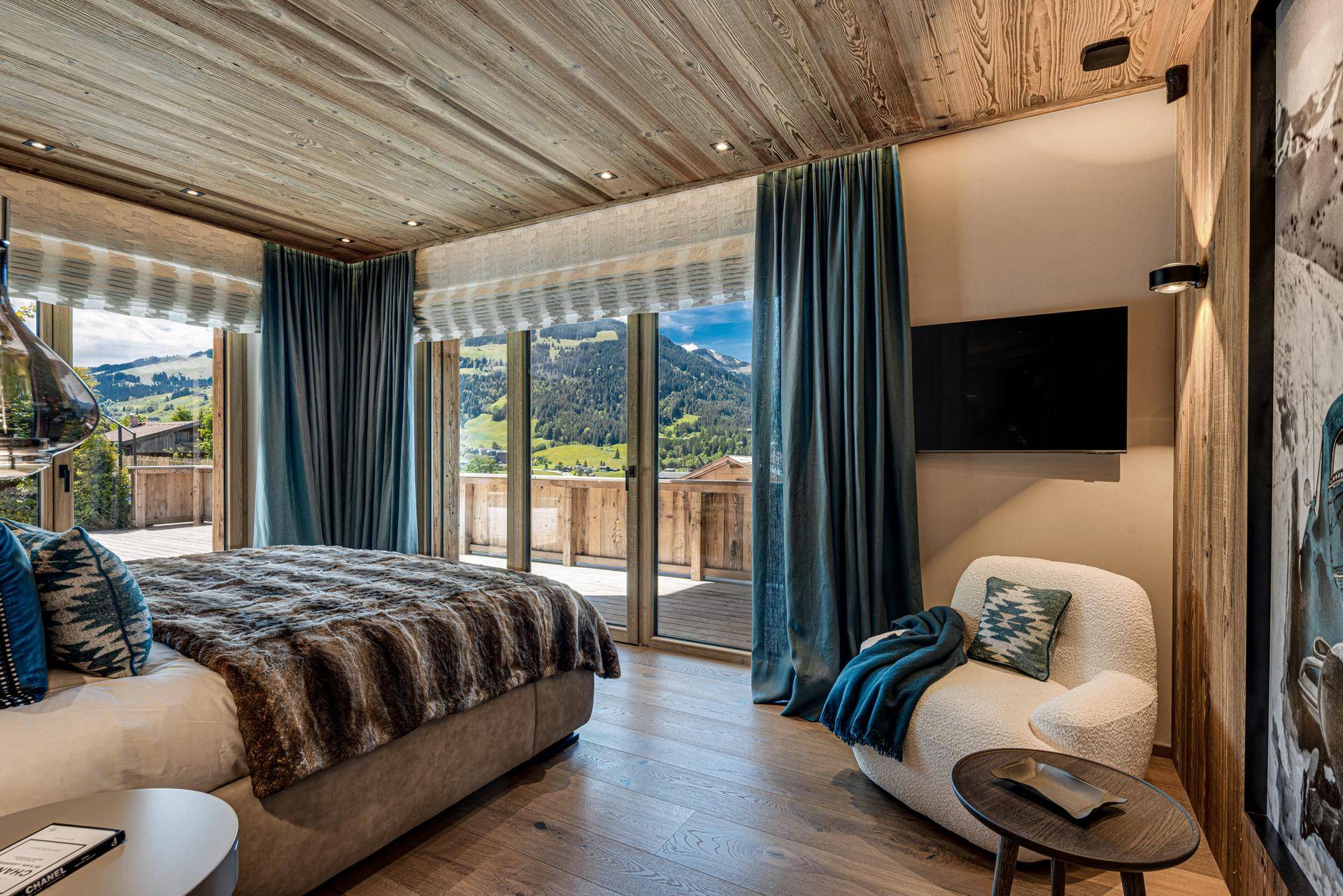 Helles Schlafzimmer mit Holzwänden, Zugang zum Balkon und Panoramablick auf die umliegenden Berge.