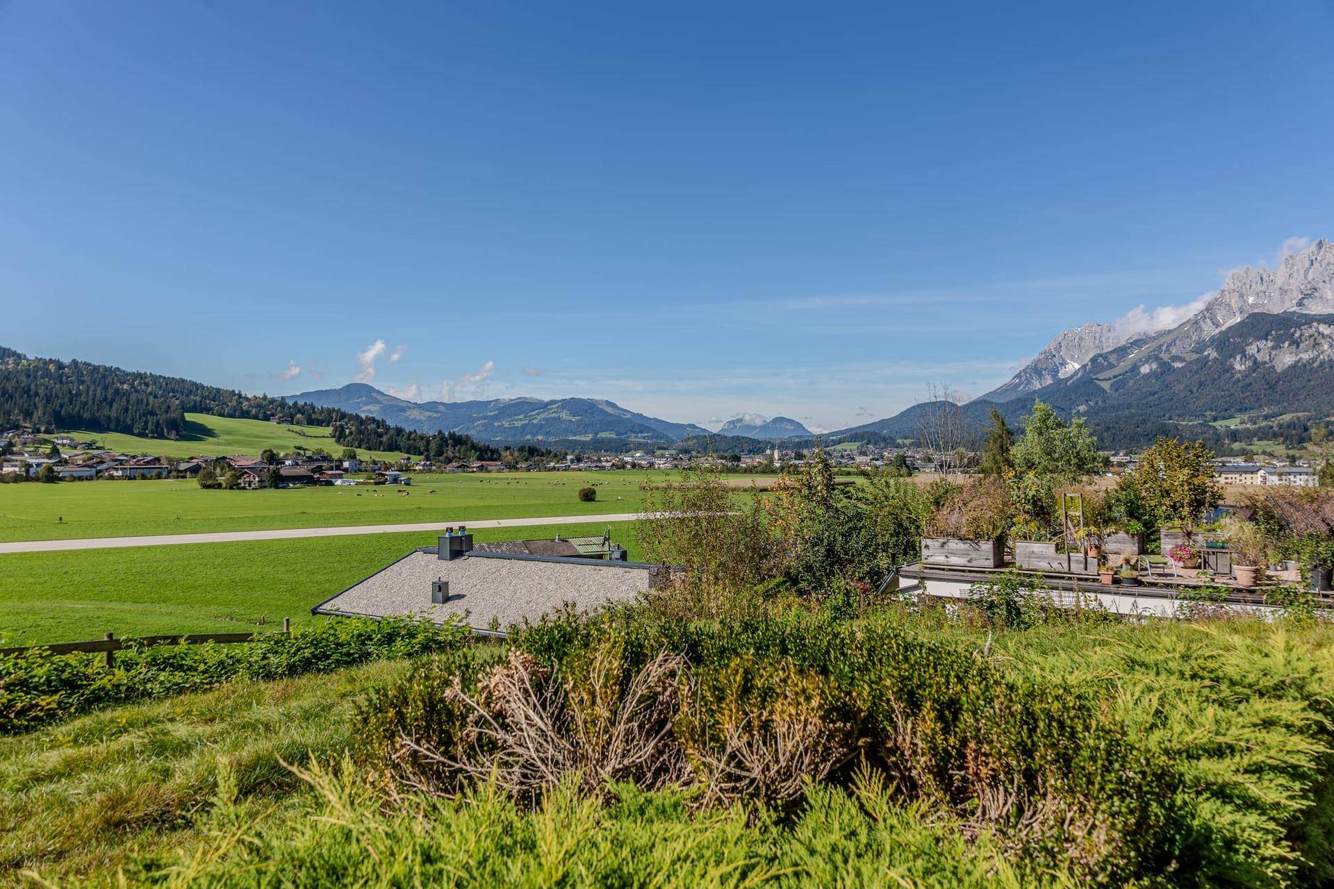 Weitläufige grüne Wiesen mit einem Haus im Vordergrund und einer beeindruckenden Bergkulisse am Horizont.